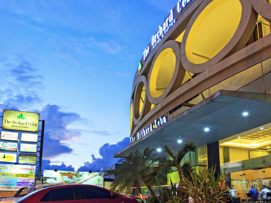 A hotel with a distinctive circular architectural design, a red car parked in front, and multiple signs advertising various services and promotions.
