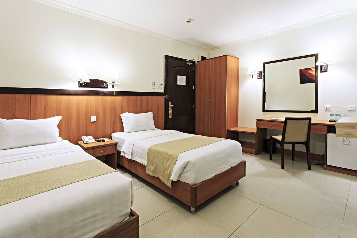 A hotel room with two beds, a desk, a chair, a wardrobe, and a mirror.