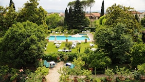 Un área de piscina rodeada de exuberante vegetación, con varias sillas de descanso y sombrillas.