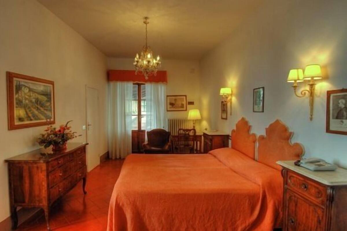 A hotel room with a large bed, a wooden dresser, a desk, a chair, and a chandelier.