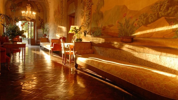 Un lobby imponente con techo alto, un candelabro y un mural que representa un paisaje montañoso.