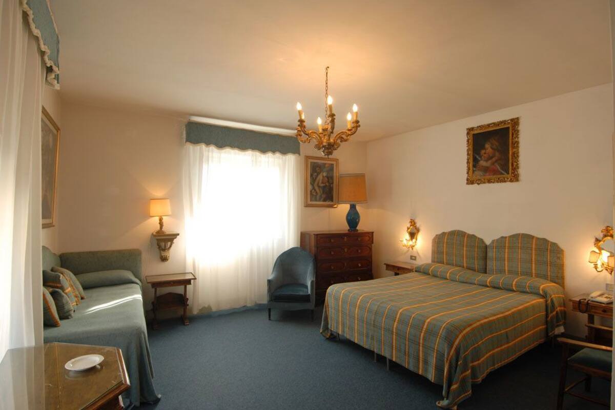 A hotel room with a bed, a chair, a desk, a dresser, and a lamp.