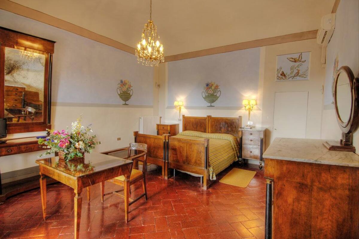 A bedroom with a wooden bed, a wooden desk, a chair, a chandelier, and two wall-mounted lamps.