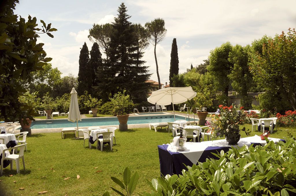 Area piscina all'aperto con lettini e ombrelloni, immersa nel verde e alberi.