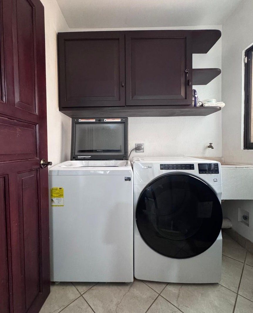 A compact laundry area with a washing machine and dryer, a dark wooden cabinet above, and a white sink.