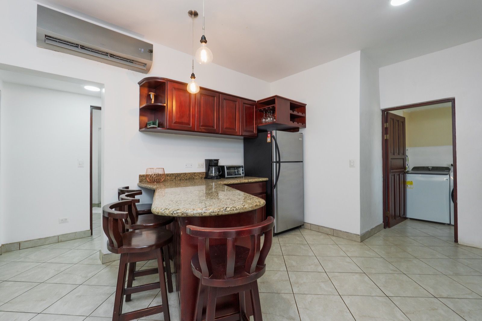 A kitchen with a granite countertop, wooden bar stools, a stainless steel refrigerator, and a built-in oven.