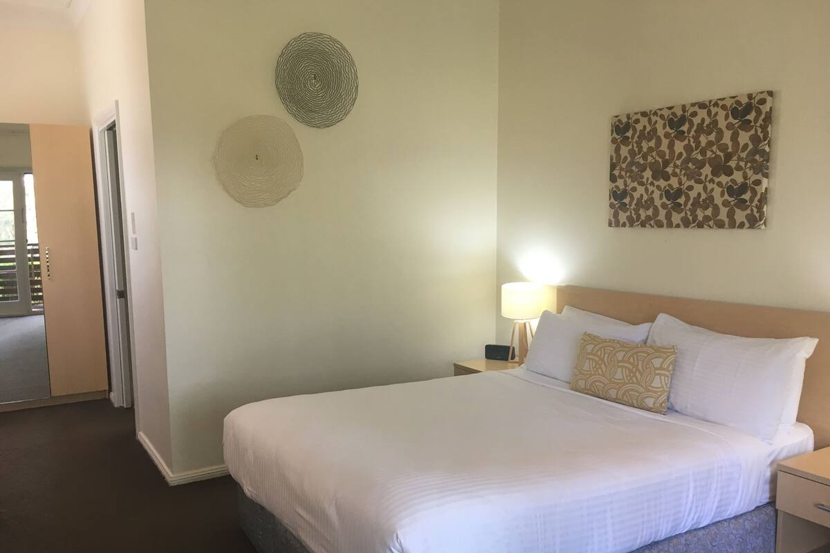 Une chambre d’hôtel avec un grand lit, une lampe de chevet, une horloge murale et une porte donnant sur un balcon.