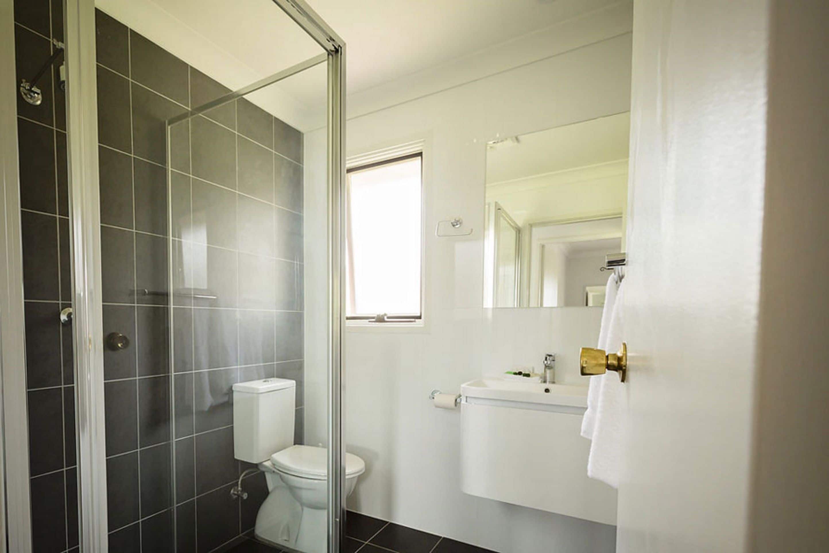 A bathroom with a glass shower enclosure, a toilet, and a sink with a mirror above it.
