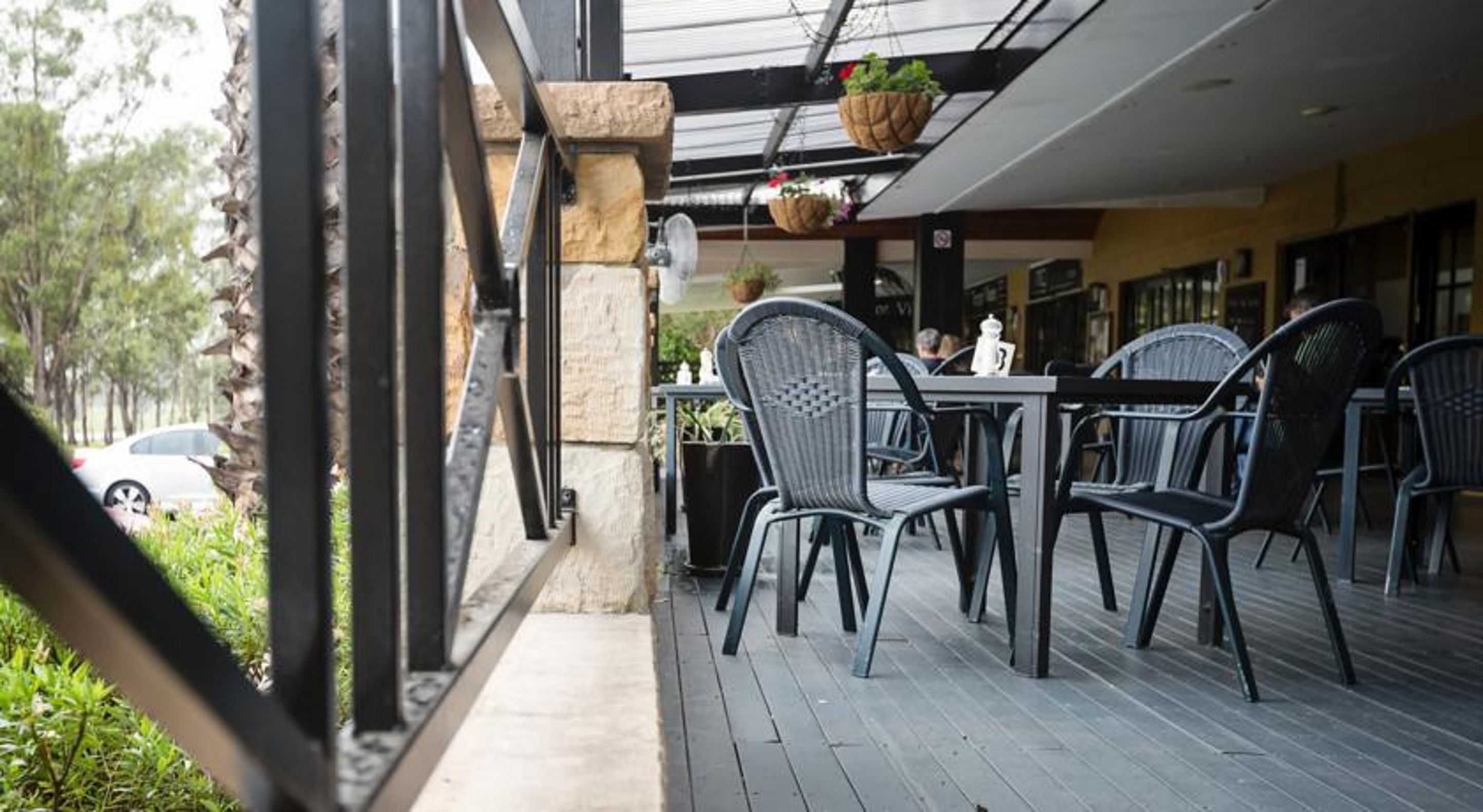 Un'area salotto all'aperto con sedie e tavoli in vimini, un pilastro in pietra e fioriere pensili.
