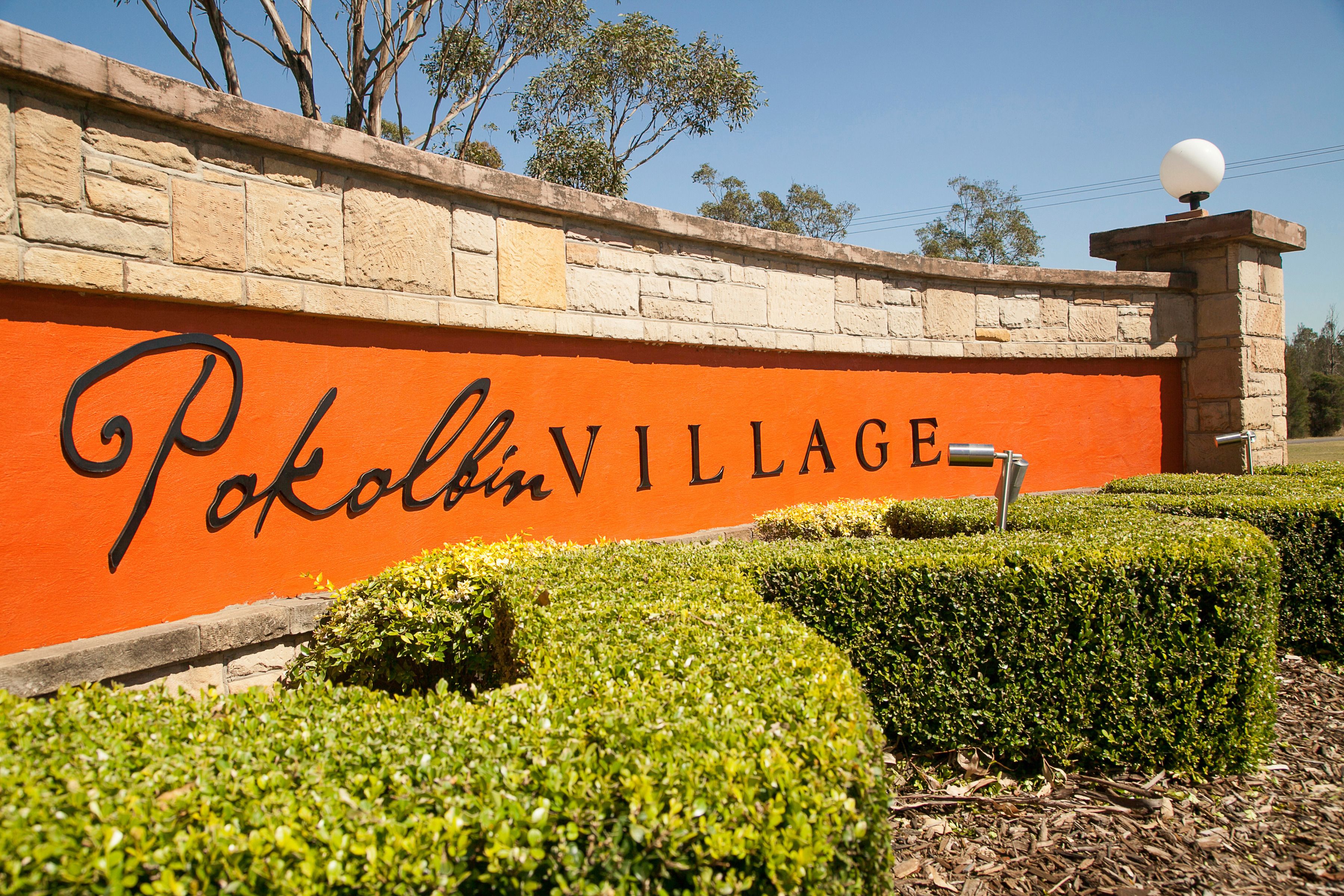 A sign for Pokolbin Village with a stone wall and neatly trimmed hedges.