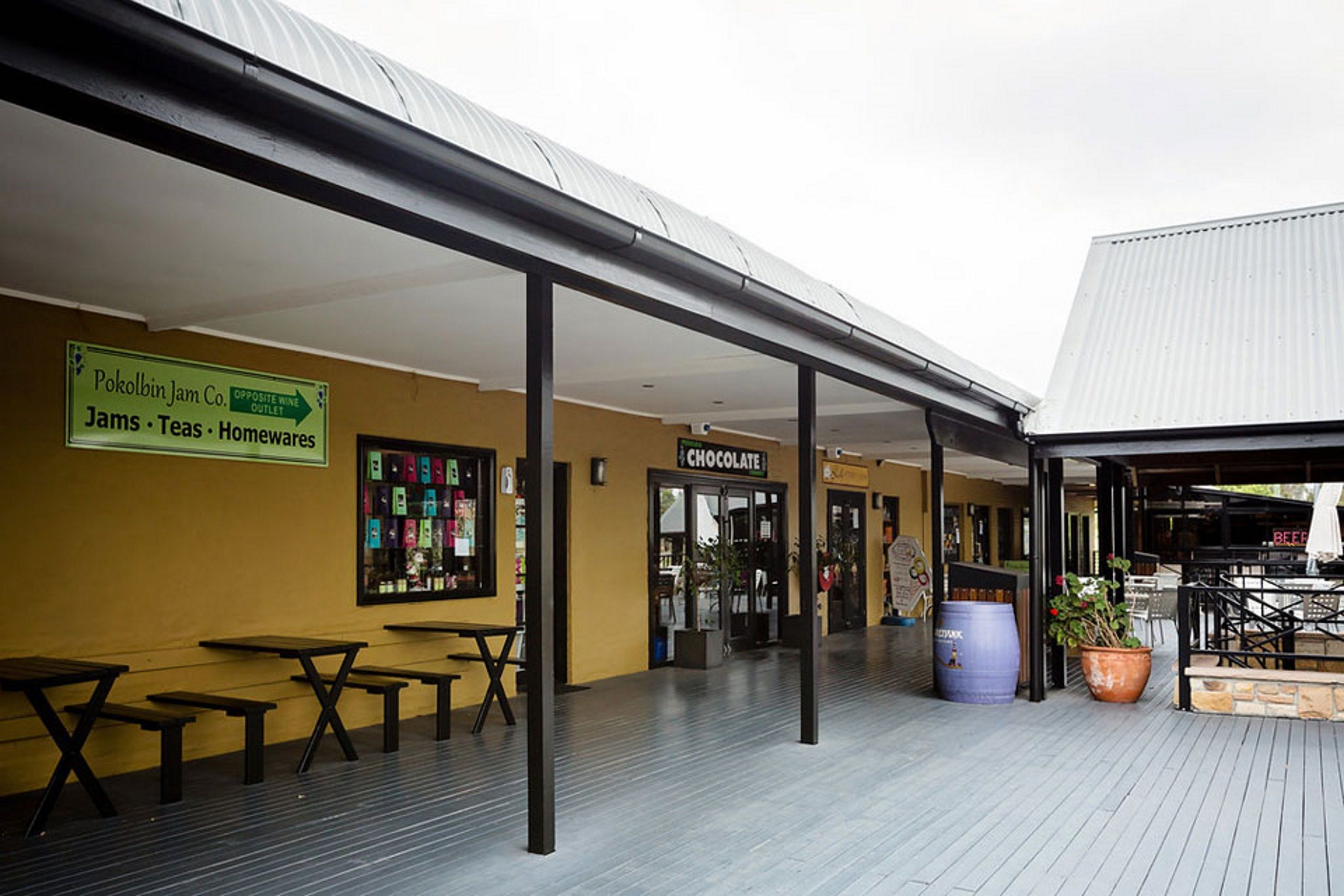 An outdoor seating area with tables and benches, a sign for Pokolbin Jam Co., and a chocolate shop.