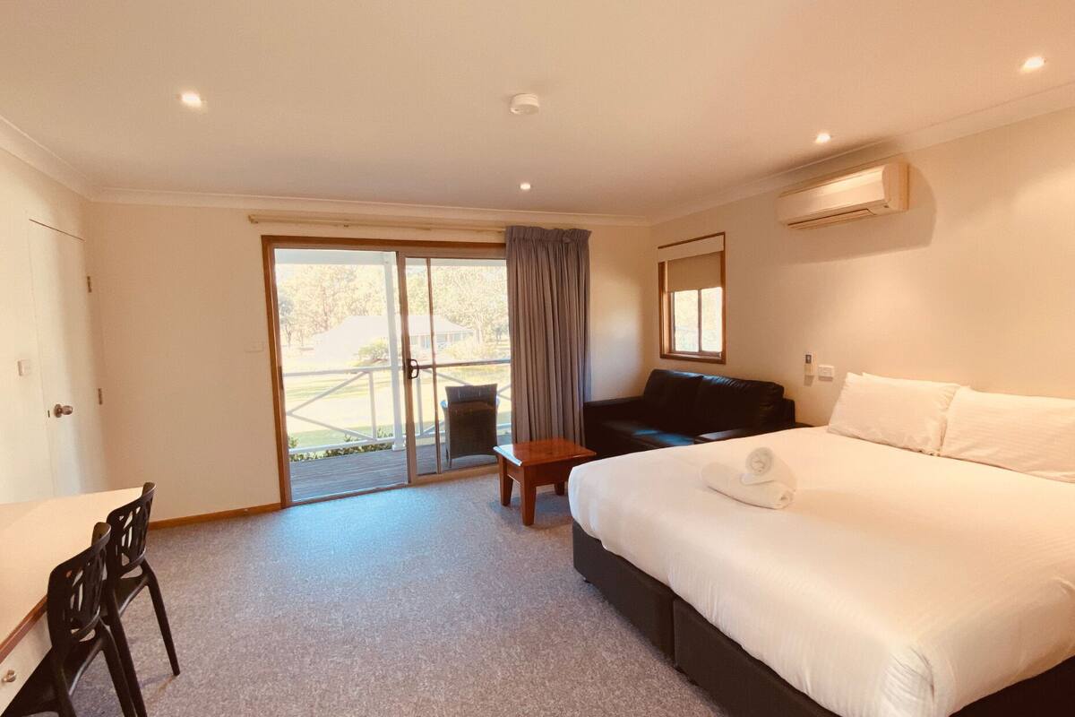 Une chambre d’hôtel comprenant un lit, un bureau, une chaise, un canapé et une porte-fenêtre coulissante donnant sur un espace extérieur.