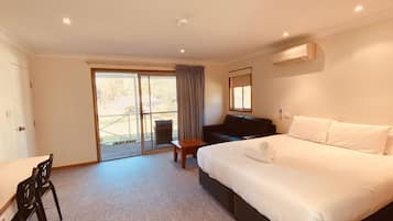 A hotel room with a bed, a desk, a chair, a sofa, and a sliding glass door leading to an outdoor area.