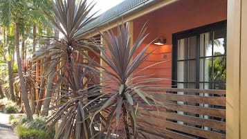 Un edificio con fachada roja, cerca de madera y plantas grandes al frente.