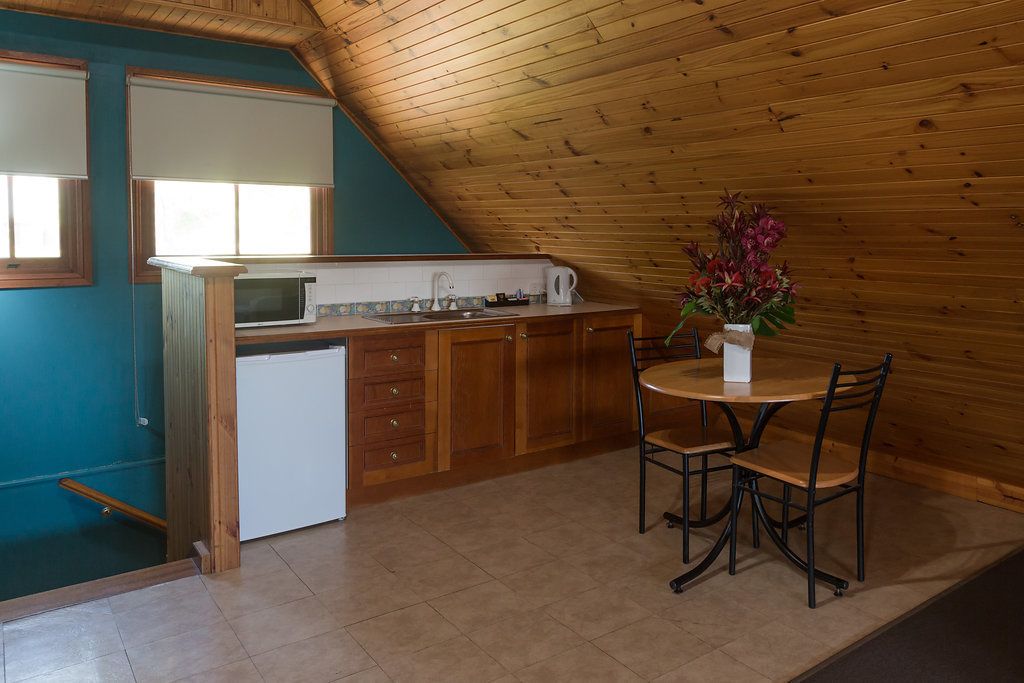Una cocina con armarios de madera, un refrigerador blanco, un microondas y un fregadero. Hay una mesa de comedor con sillas y un jarrón con flores.