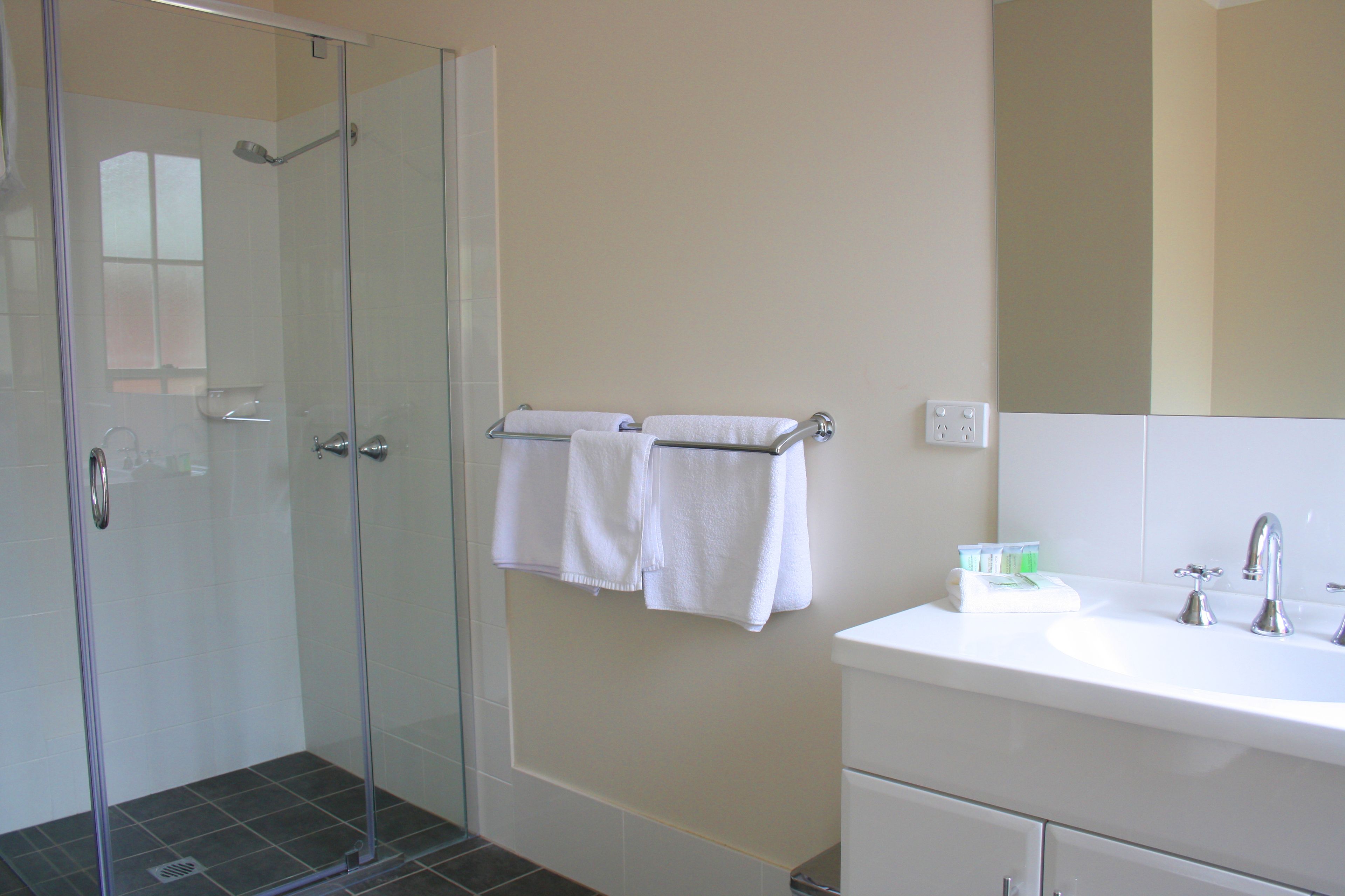 Un baño con cabina de ducha de vidrio, un lavabo blanco y un perchero con dos toallas.