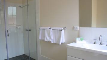 Un baño con cabina de ducha de vidrio, un lavabo blanco y un perchero con dos toallas.