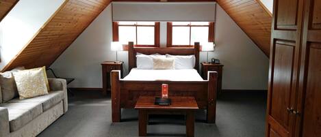 Une chambre avec un plafond en bois, un lit avec une literie blanche, une table de chevet, une lampe, une armoire en bois et un canapé agrémenté de coussins à motifs.