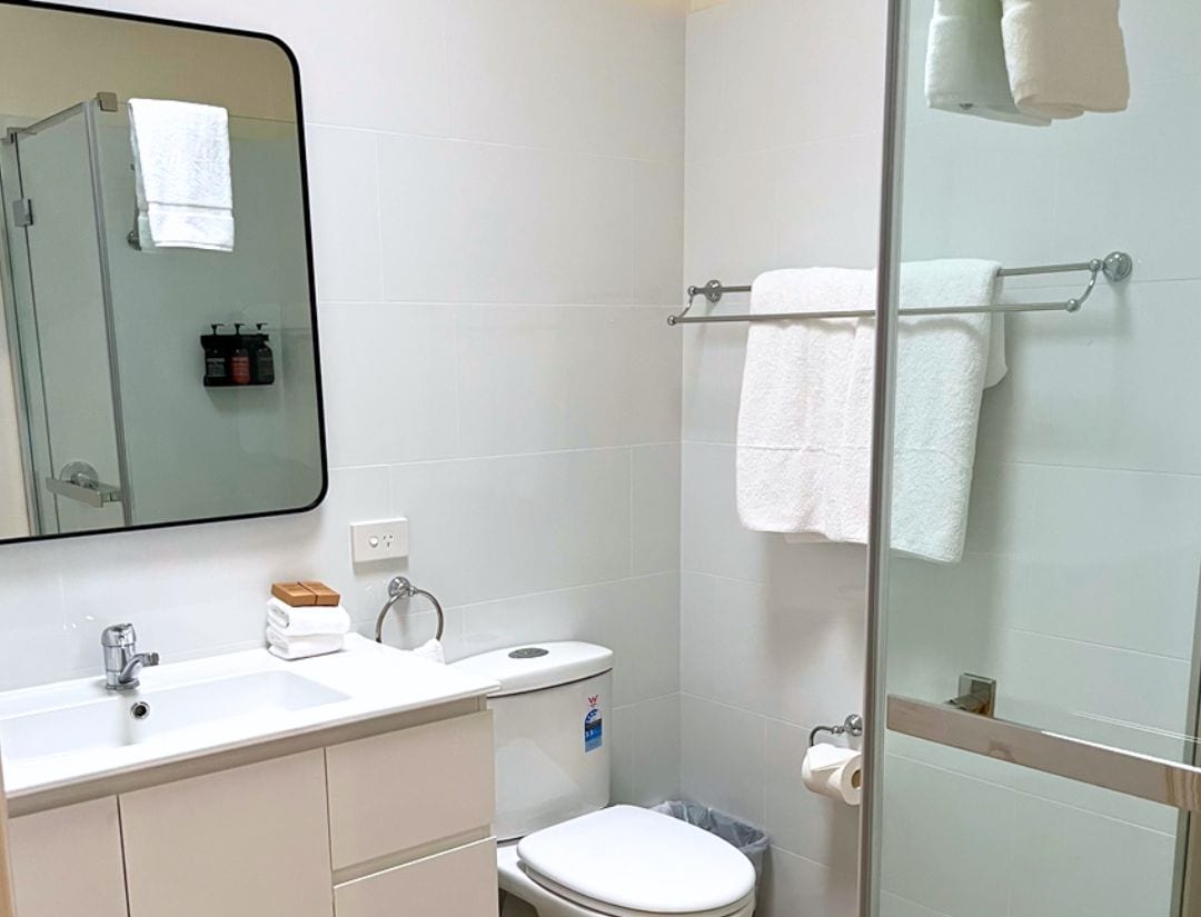 A bathroom with a white sink, mirror, and toilet. There are towels hanging on a rack and a glass shower door.