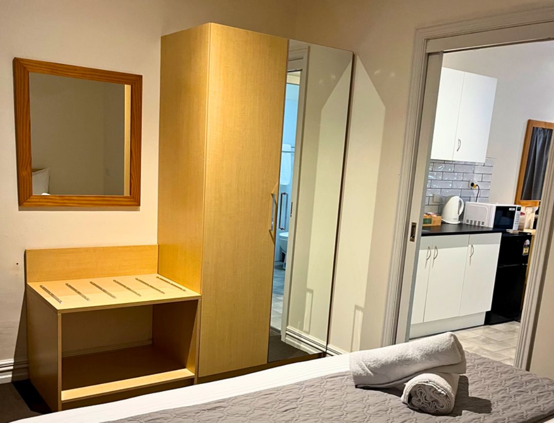 A Deluxe King Suite with a bed, a wooden bench, a wardrobe, and a mirror.