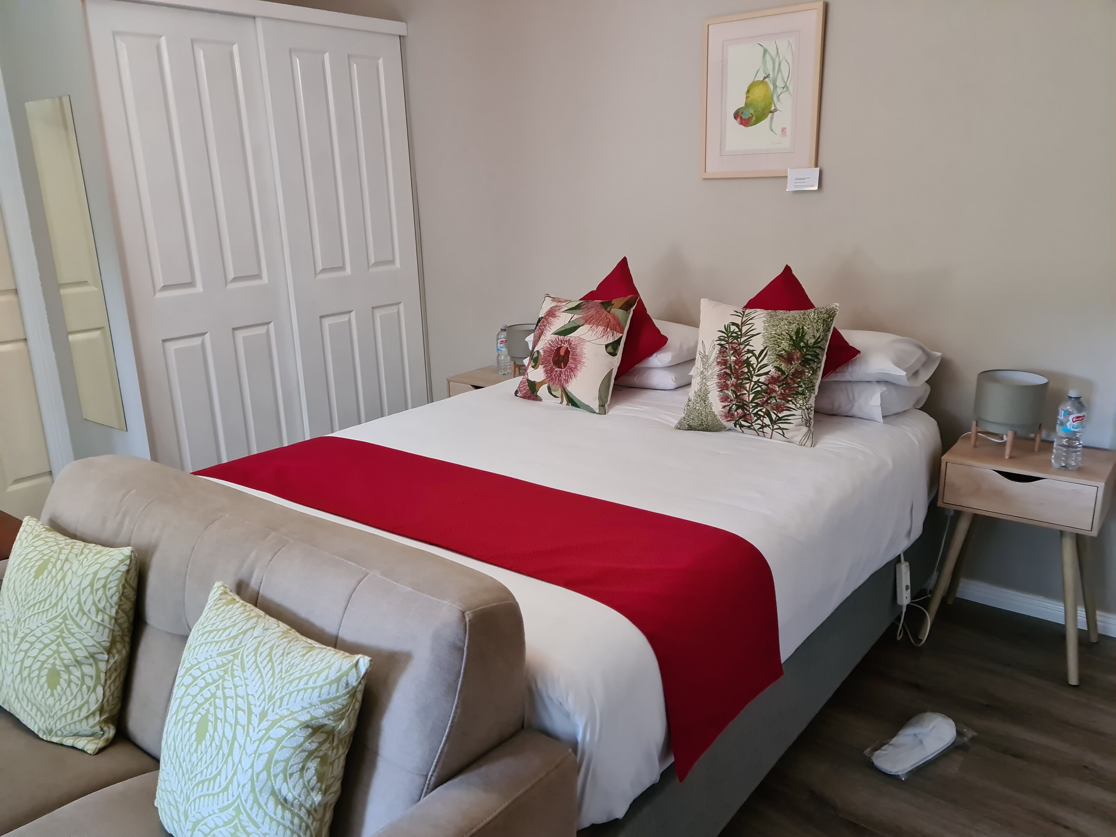A hotel room with a bed, a nightstand, a lamp, a bottle of water, and a pair of slippers.