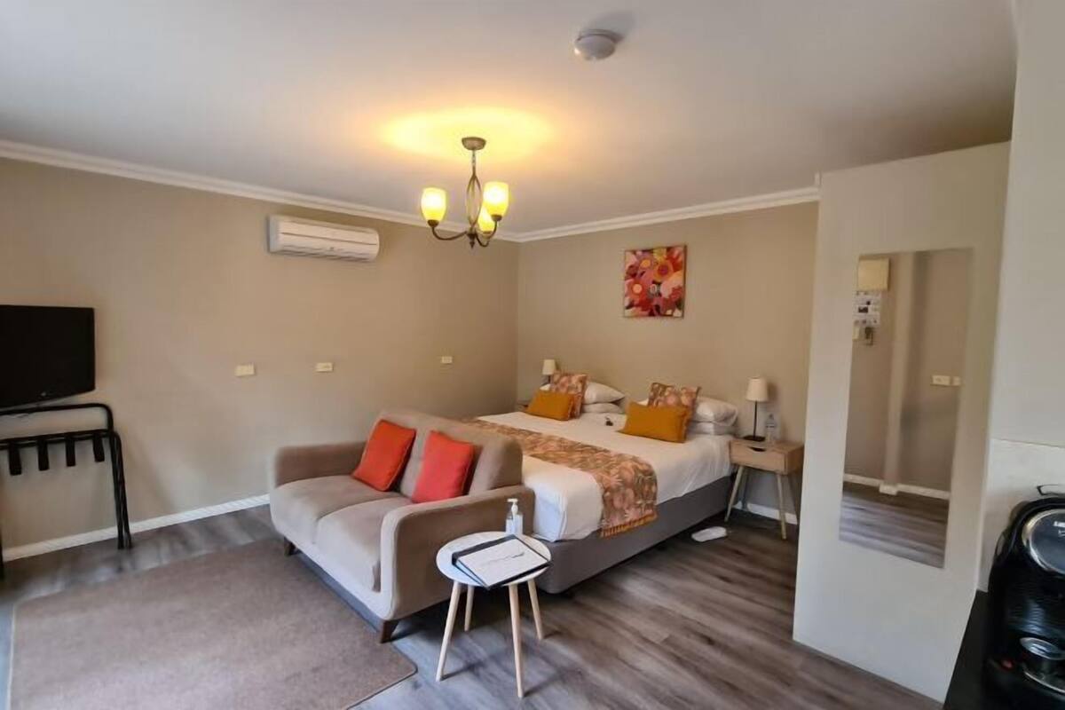 A hotel room with a bed, a sofa, a small table, a TV, and a mirror.