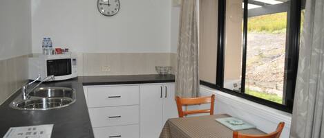 Una cocina compacta equipada con microondas, lavamanos y un comedor con mesa y sillas.