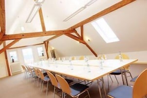 Una sala de conferencias con una larga mesa, sillas y un techo inclinado con vigas de madera.