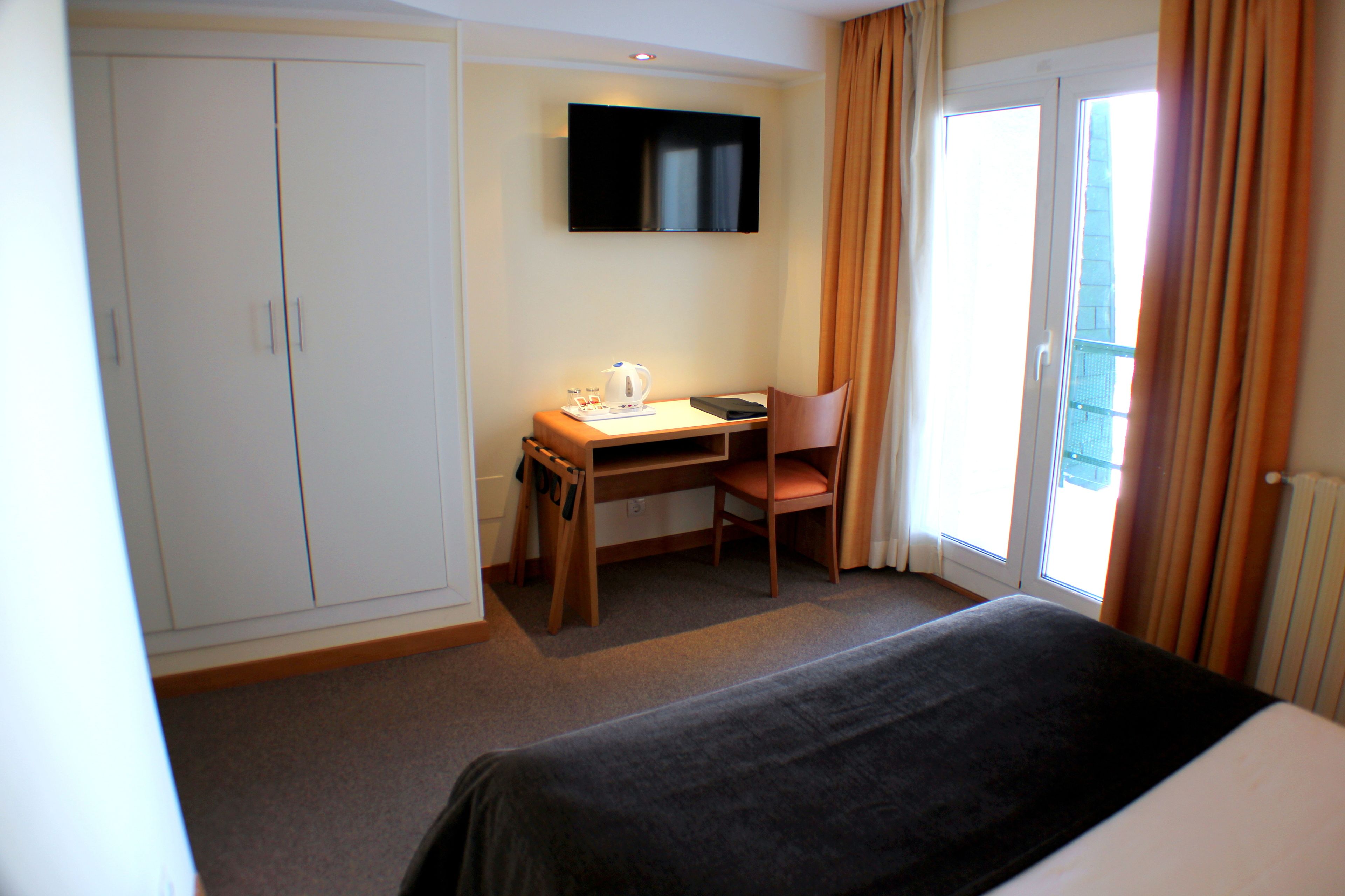 A hotel room with a bed, a desk with a chair, a television, and a wardrobe.