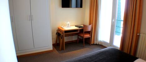 A hotel room with a bed, a desk with a chair, a television, and a wardrobe.
