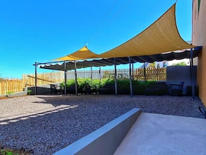 A covered outdoor area with a gravel ground, a wooden fence, and outdoor furniture.