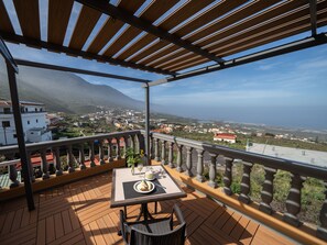 A balcony with a table and chairs, overlooking a coastal town and mountains. - Hotel Ida Inés (Frontera)