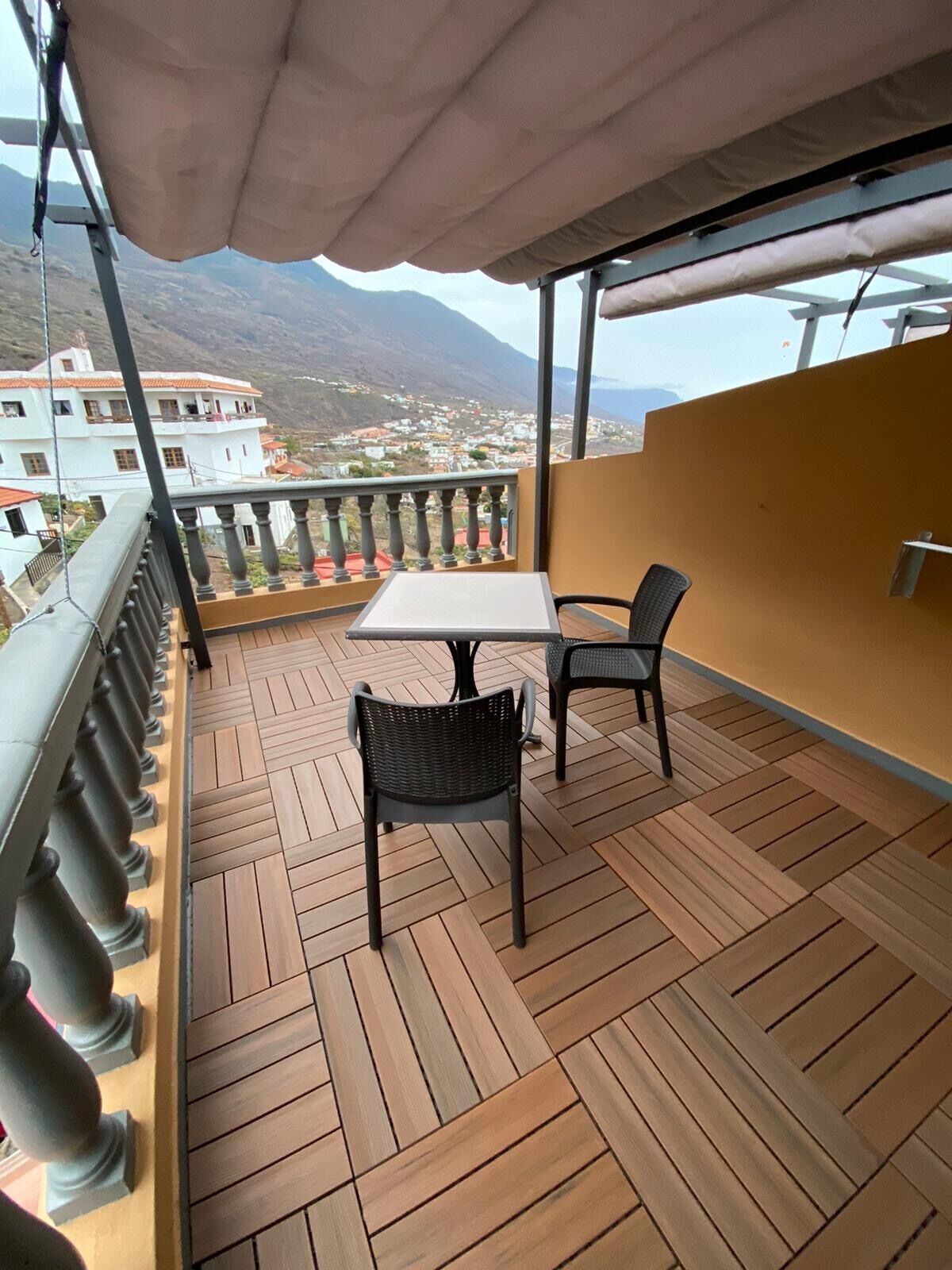 Un balcón con una mesa y dos sillas, con vistas a un paisaje montañoso.