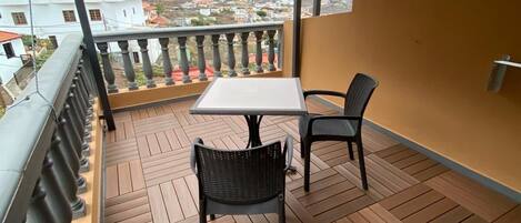 Un balcón con una mesa y dos sillas, con vistas a un paisaje montañoso.