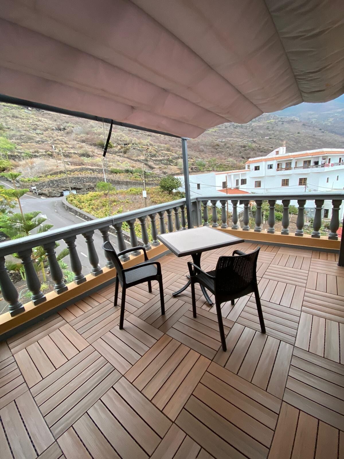 Un balcon avec une table et des chaises, donnant sur une rue et un immeuble.