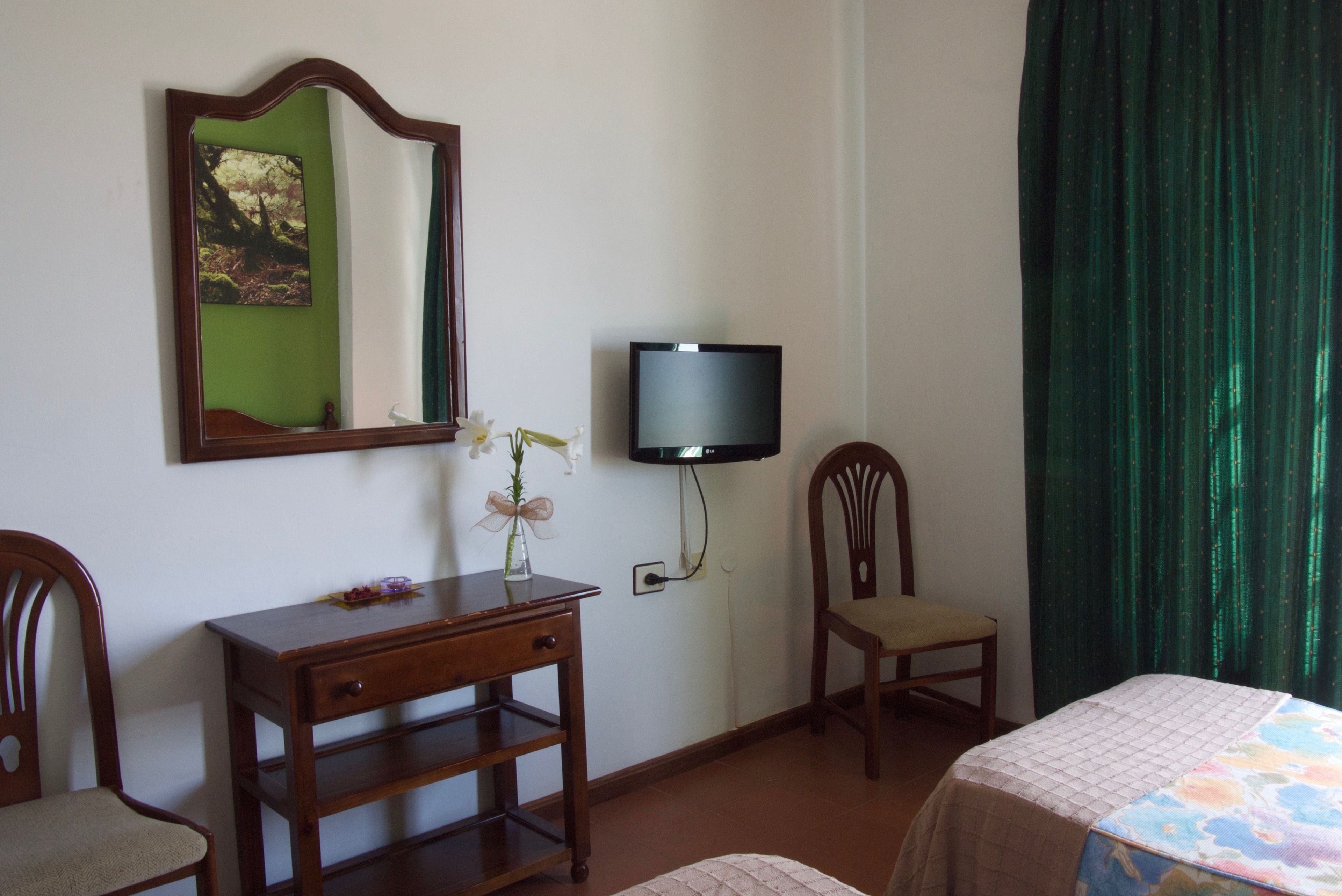 A hotel room with a wooden desk, a chair, a television, and a bed with a quilted cover.