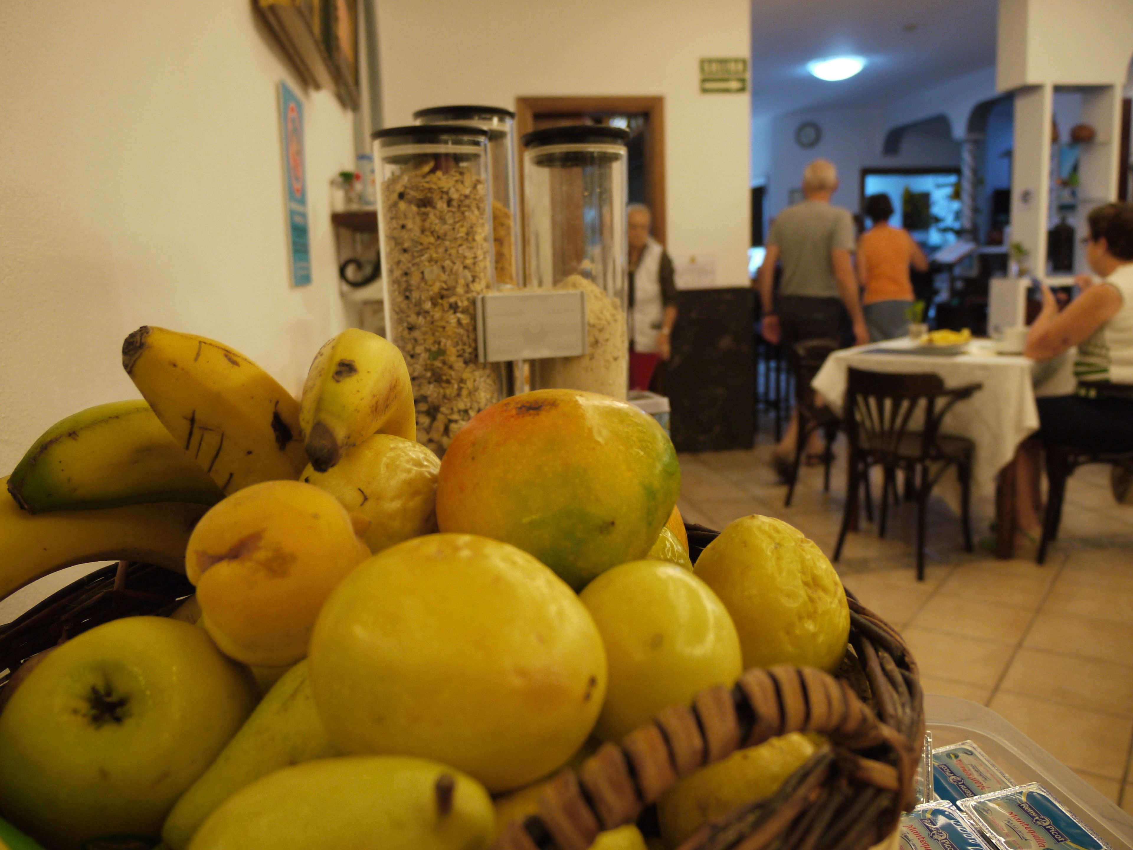 A fruit display with bananas and lemons in a basket, a coffee machine, and a dining area with tables and chairs.