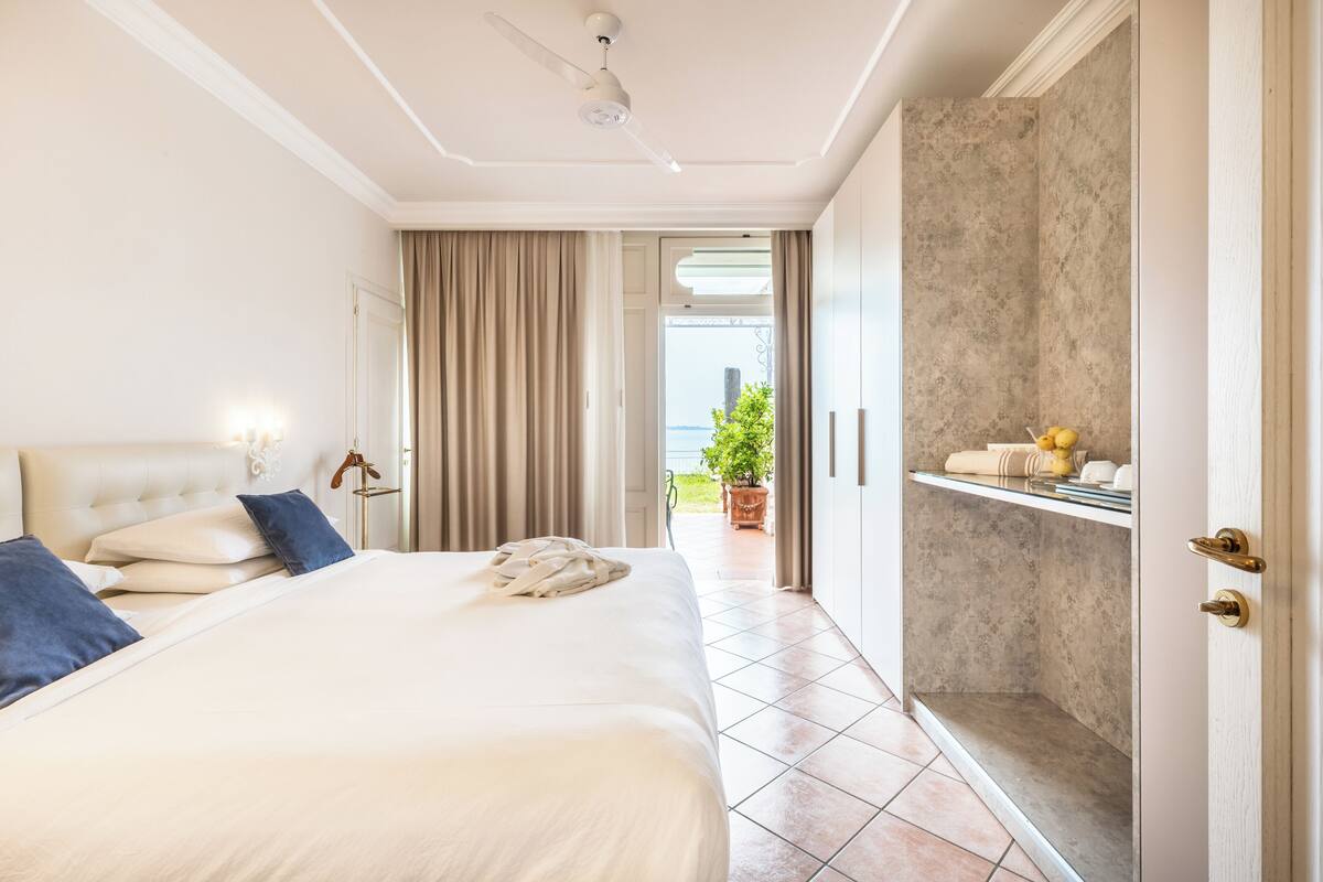 A hotel room with a large bed, a ceiling fan, a bathroom with a shower, and a view of the outdoors.