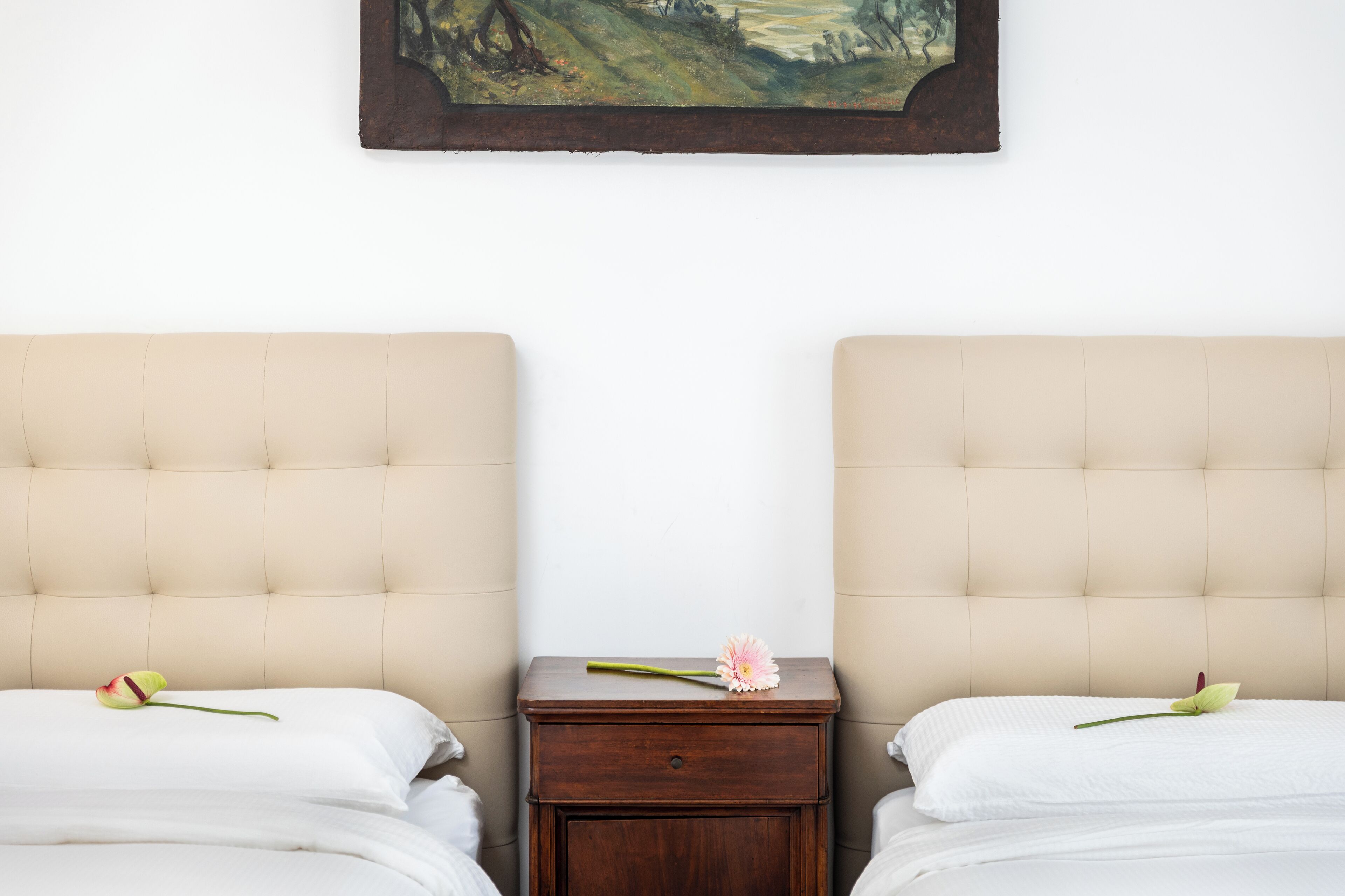 Een hotelkamer met twee bedden, een klein houten nachtkastje ertussen en een schilderij erboven.