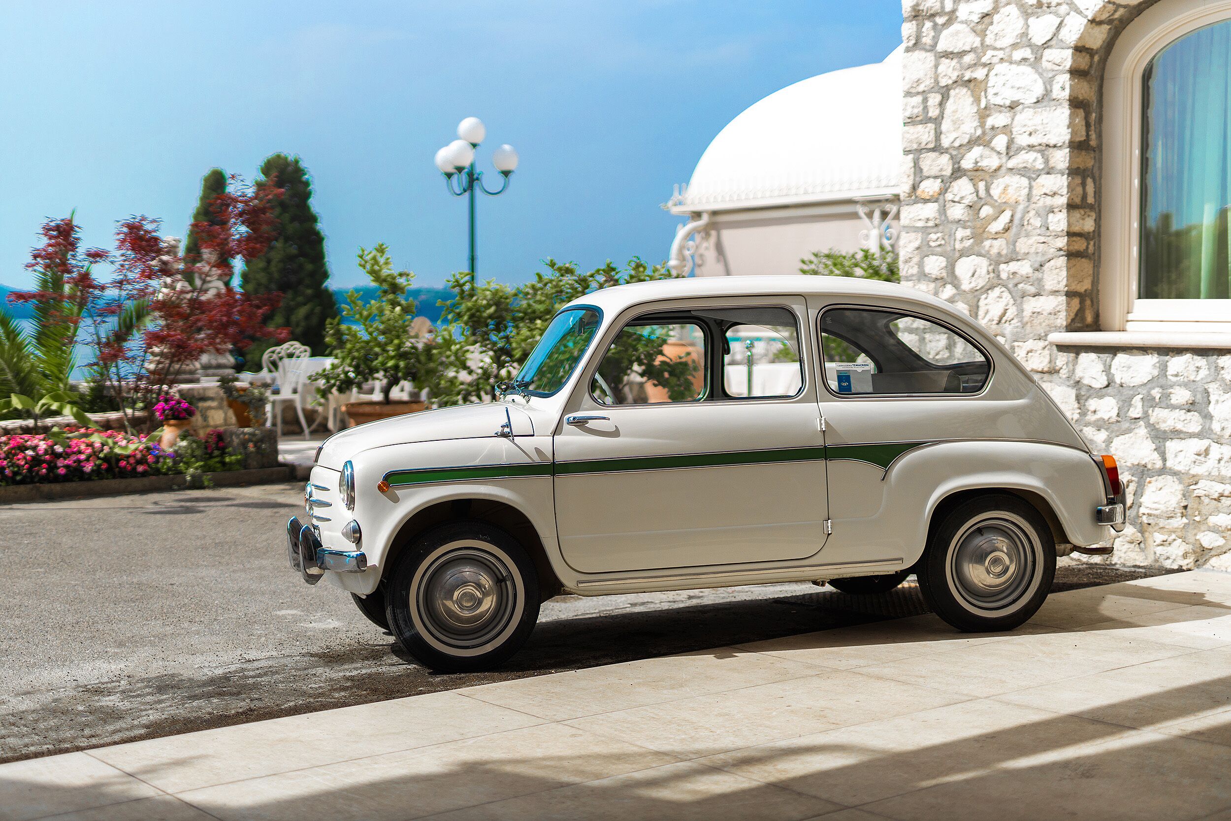 Une voiture blanche ancienne est garée devant un bâtiment en pierre surmonté d’un dôme blanc.