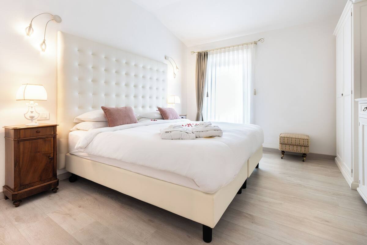 A bedroom with a large bed, a nightstand, a small stool, and a wardrobe.