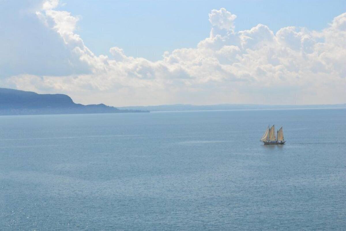 A calm sea with a sailboat in the distance, a clear sky, and distant landforms.