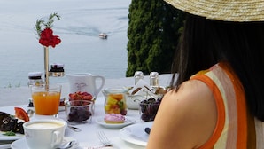 Una mesa dispuesta con alimentos para el desayuno, un sombrero de paja y vistas al mar.