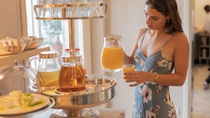 Una disposición de bufé con un expositor de vidrio escalonado, una jarra de jugo de naranja y diferentes platos en una bandeja.