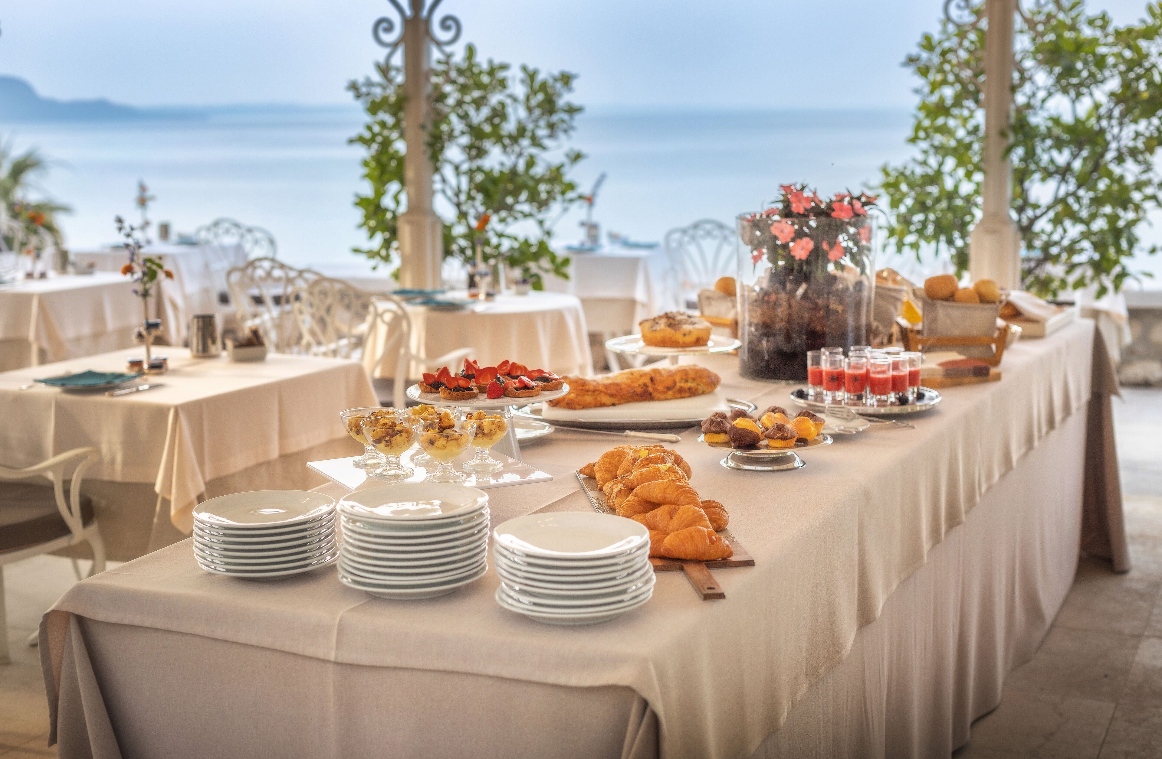 A buffet table with various food items and a view of the sea.