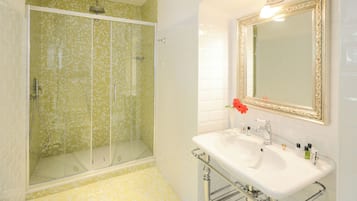 A bathroom with a glass-enclosed shower, a white sink with a mirror, and a tiled floor.