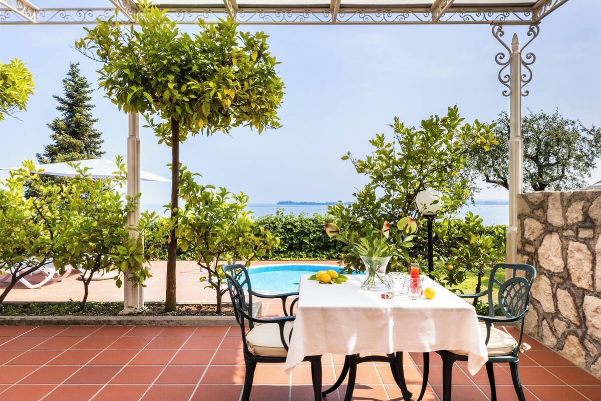 A terrace with a table set for two, overlooking a pool and a scenic view.