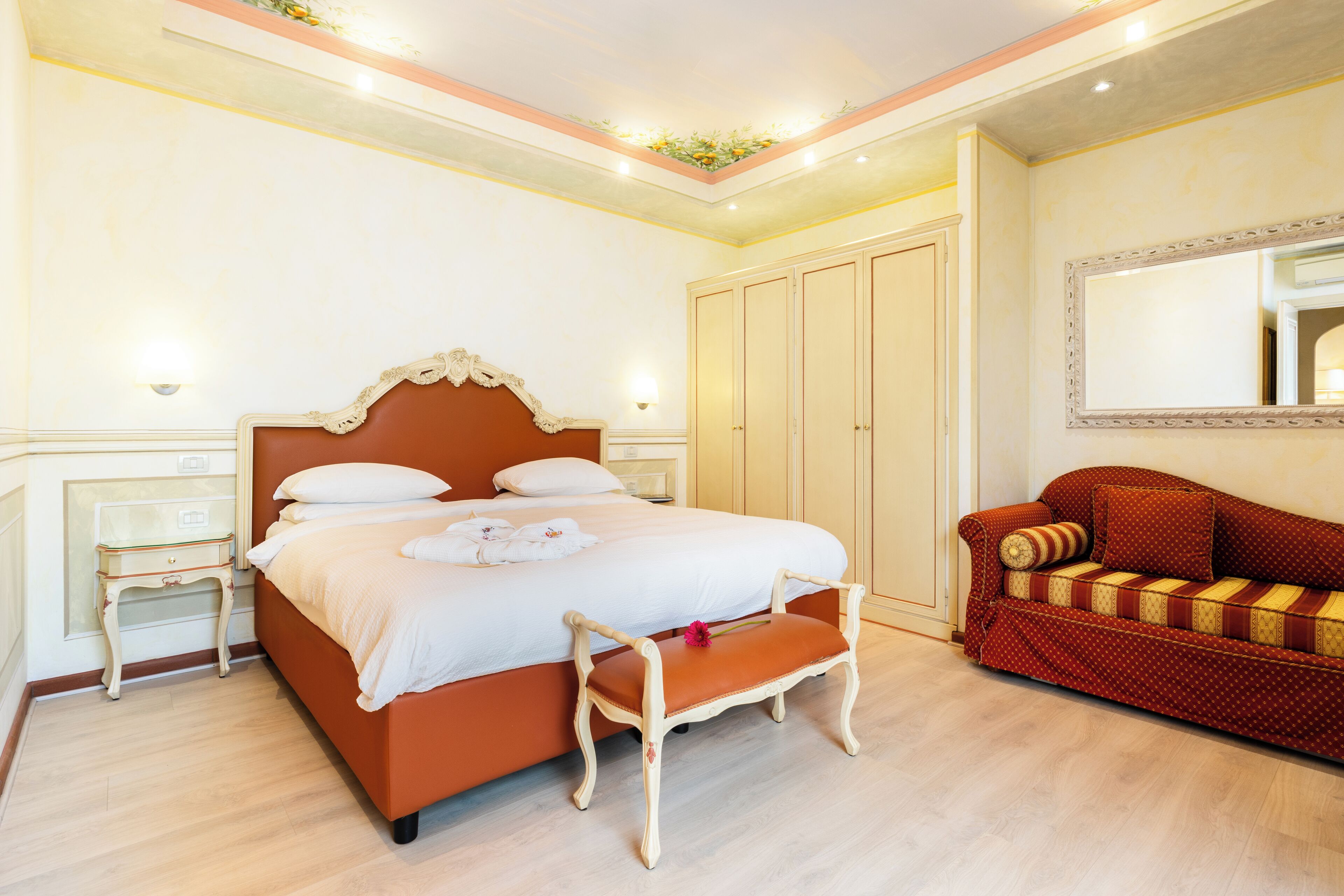 A bedroom with a large bed, a wooden bench, a red sofa, and a wardrobe.
