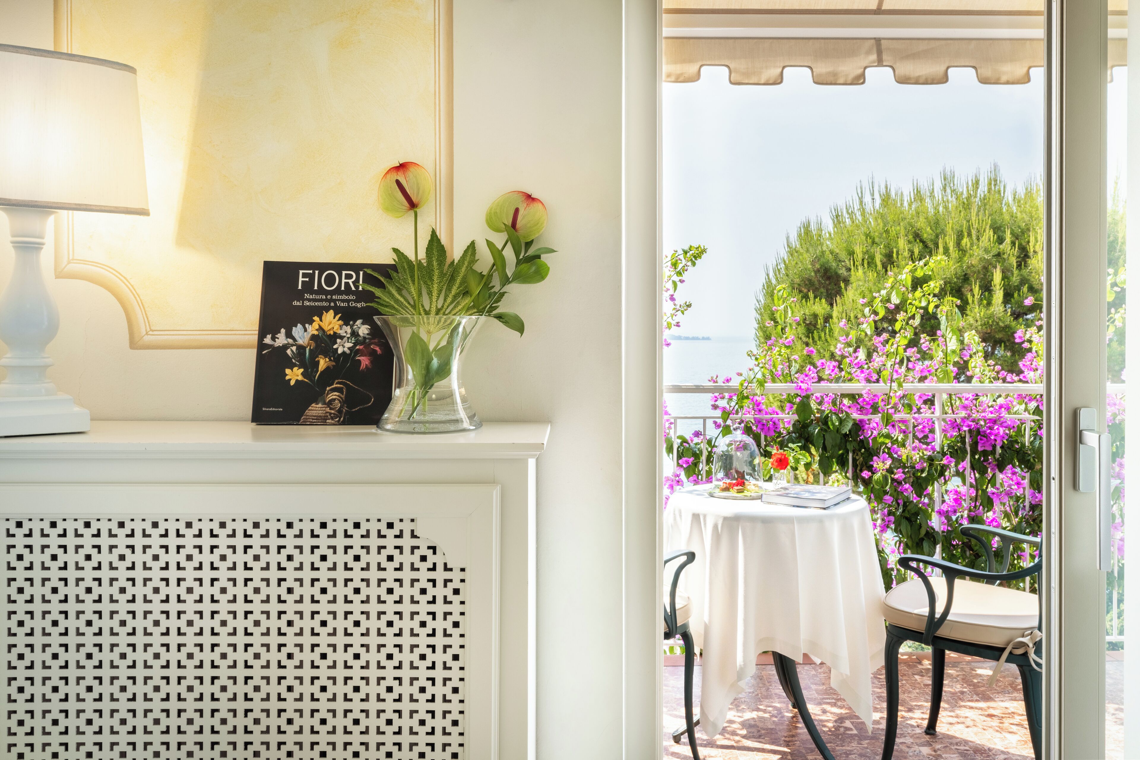 A room with a white console table, a book titled 'Fiori,' and a vase with flowers.
