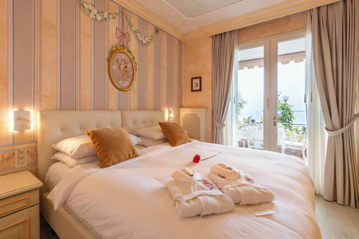 A hotel room with a large bed, a nightstand, a wall-mounted picture, and a view of the outdoors through a door.